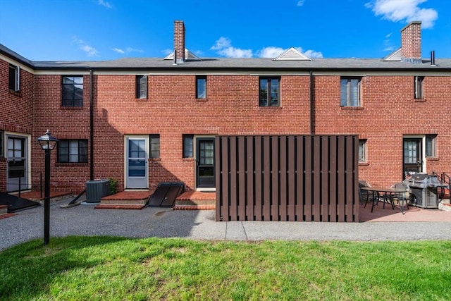 back of property with a chimney, a patio area, brick siding, and central AC unit