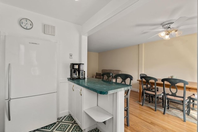 kitchen with freestanding refrigerator, a peninsula, a breakfast bar area, light wood-style flooring, and dark countertops