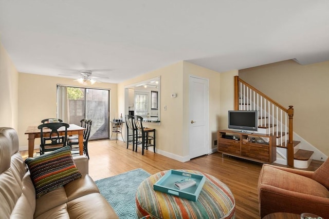 living room with stairway, wood finished floors, ceiling fan, and baseboards