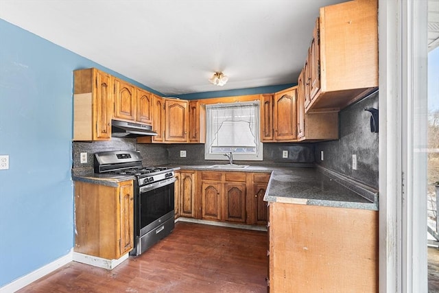 kitchen featuring brown cabinets, backsplash, a sink, under cabinet range hood, and stainless steel gas range oven