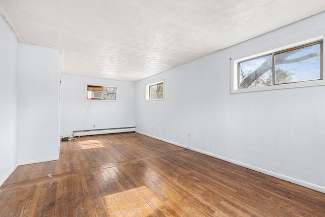 empty room featuring hardwood / wood-style flooring, baseboards, a baseboard heating unit, and an AC wall unit