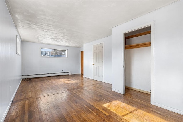 unfurnished bedroom with wood-type flooring, baseboards, and baseboard heating