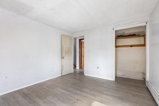 unfurnished bedroom featuring a closet, baseboard heating, wood finished floors, and baseboards