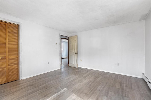 unfurnished bedroom featuring a closet, baseboard heating, wood finished floors, and baseboards