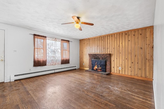 unfurnished living room with wooden walls, wood finished floors, baseboard heating, a textured ceiling, and a fireplace