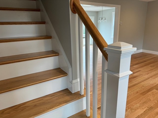 staircase with a notable chandelier, baseboards, and wood finished floors