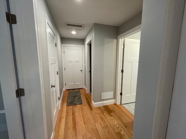 hallway with light wood-style floors, baseboards, and visible vents