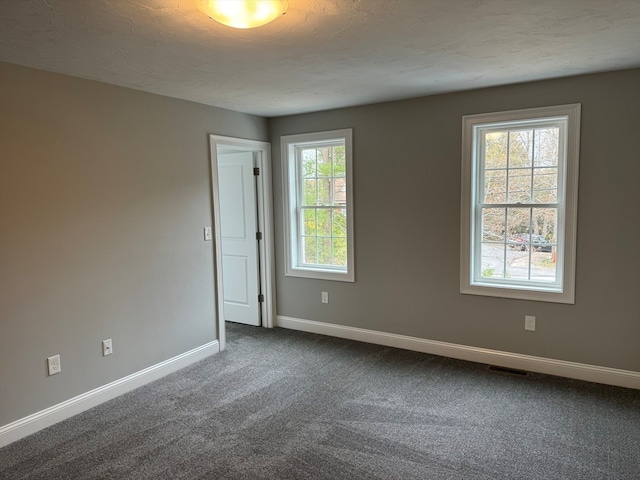 spare room featuring a textured ceiling, dark carpet, visible vents, and baseboards