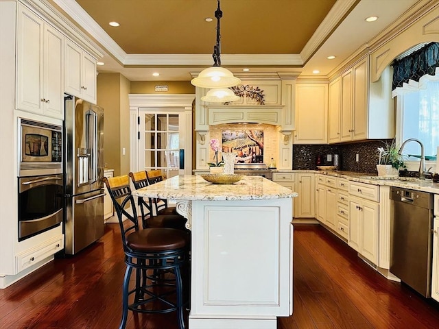 kitchen with light stone counters, a raised ceiling, appliances with stainless steel finishes, ornamental molding, and a sink