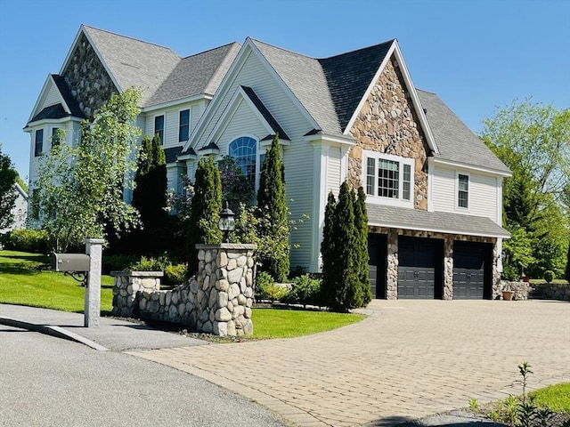 view of front of house featuring stone siding, a front lawn, decorative driveway, and an attached garage