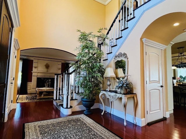 corridor with arched walkways, hardwood / wood-style flooring, a towering ceiling, baseboards, and stairs