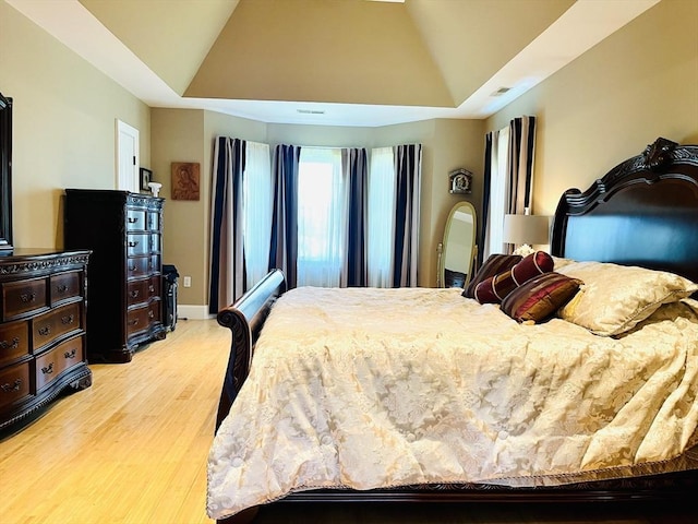 bedroom with light wood-style floors, a tray ceiling, vaulted ceiling, and baseboards