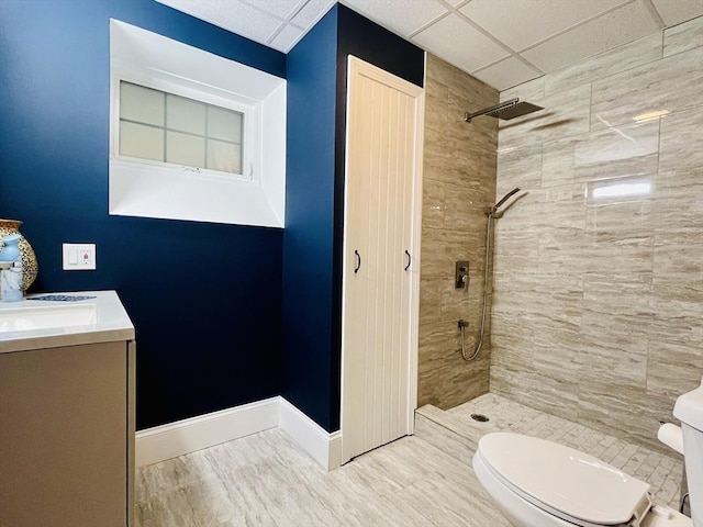 full bathroom with toilet, baseboards, a tile shower, and vanity