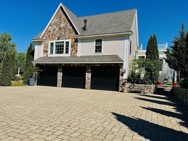 view of side of property with a garage, stone siding, and roof with shingles