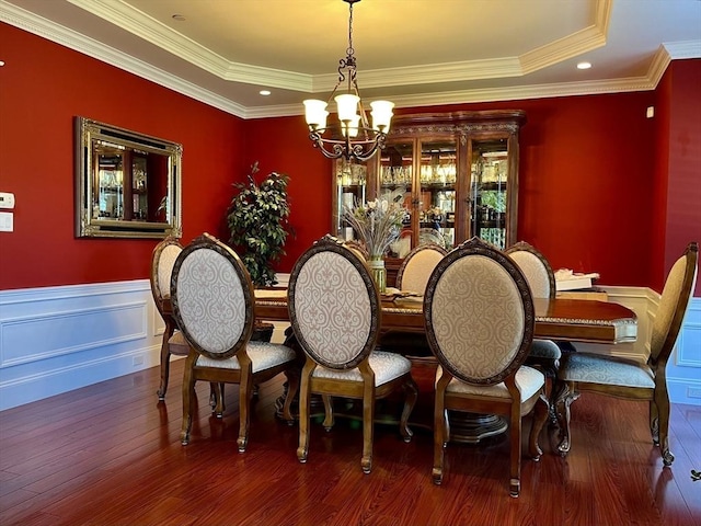 dining space featuring a wainscoted wall, wood finished floors, a tray ceiling, crown molding, and a notable chandelier