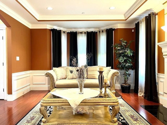 living area featuring arched walkways, wood finished floors, a wainscoted wall, and a raised ceiling