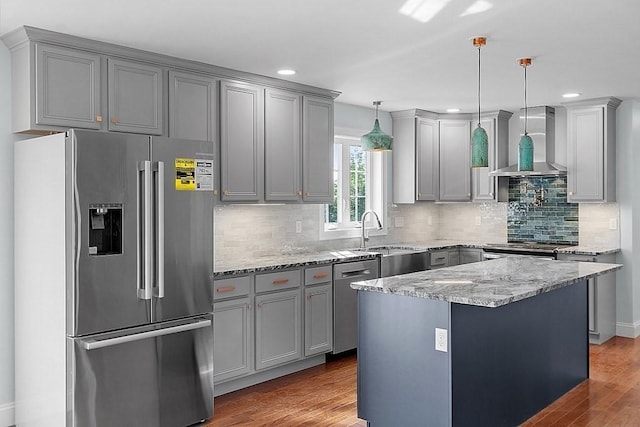 kitchen with appliances with stainless steel finishes, wall chimney exhaust hood, sink, dark hardwood / wood-style floors, and hanging light fixtures