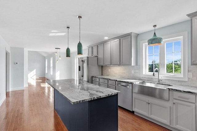 kitchen featuring appliances with stainless steel finishes, backsplash, gray cabinetry, light hardwood / wood-style floors, and a kitchen island