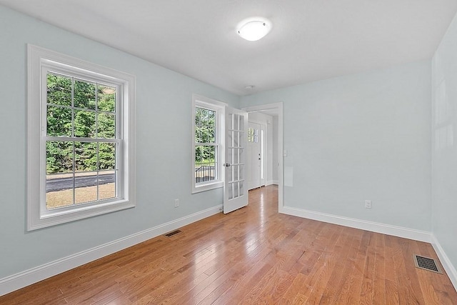 empty room featuring french doors, light hardwood / wood-style floors, and a healthy amount of sunlight