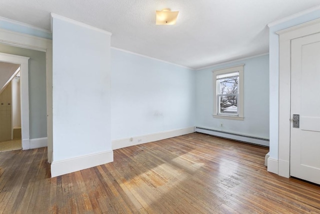 spare room with ornamental molding, baseboard heating, dark wood finished floors, and baseboards