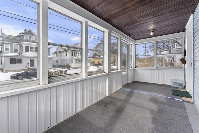 unfurnished sunroom featuring a residential view, wood ceiling, and a healthy amount of sunlight