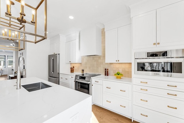 kitchen with stainless steel appliances, a sink, white cabinets, wall chimney range hood, and pendant lighting