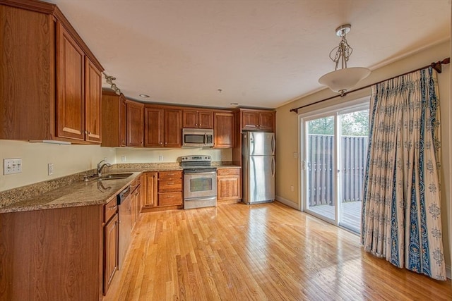 kitchen featuring light stone countertops, sink, stainless steel appliances, decorative light fixtures, and light wood-type flooring