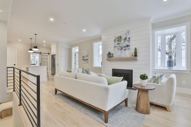 living room featuring a large fireplace, light wood-type flooring, ornamental molding, and a wealth of natural light