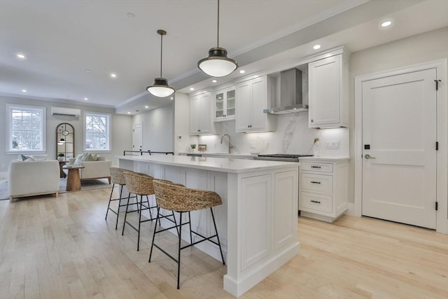 kitchen featuring a wall unit AC, a center island, decorative light fixtures, wall chimney range hood, and white cabinetry