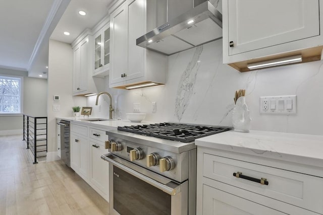 kitchen featuring sink, white cabinetry, high end stove, wall chimney exhaust hood, and light stone countertops