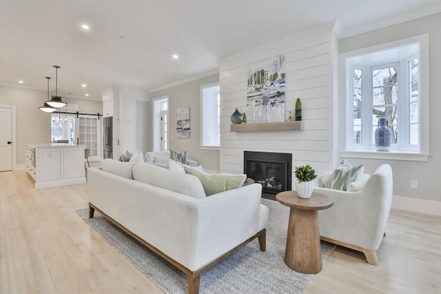 living room featuring crown molding, a large fireplace, light hardwood / wood-style floors, and a barn door