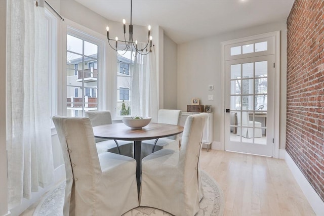 dining space featuring brick wall, light hardwood / wood-style floors, and a chandelier