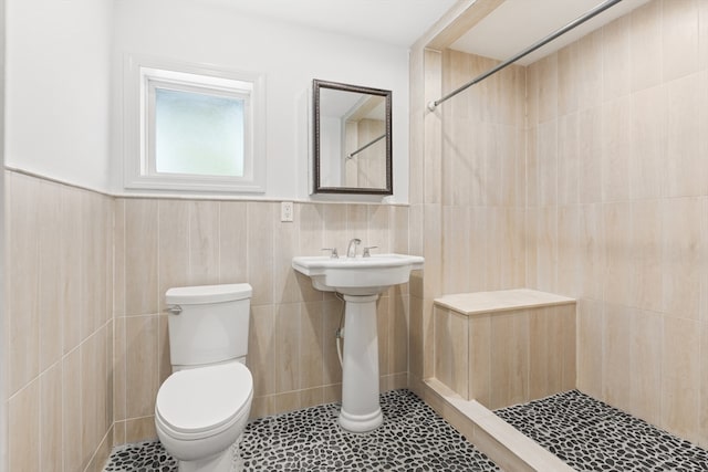 bathroom with toilet, tiled shower, tile patterned flooring, and tile walls