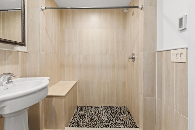 bathroom with a tile shower, sink, and tile walls