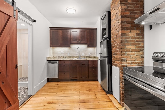 kitchen featuring sink, light stone countertops, ventilation hood, light wood-type flooring, and appliances with stainless steel finishes