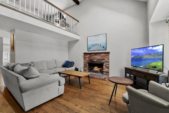 living room with hardwood / wood-style floors, beamed ceiling, a brick fireplace, and a high ceiling