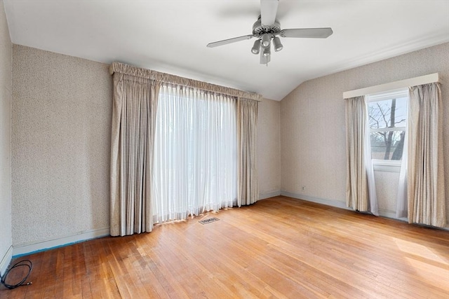 spare room featuring wallpapered walls, baseboards, lofted ceiling, hardwood / wood-style floors, and a ceiling fan