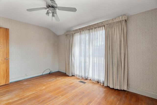 spare room featuring visible vents, baseboards, vaulted ceiling, hardwood / wood-style floors, and a ceiling fan