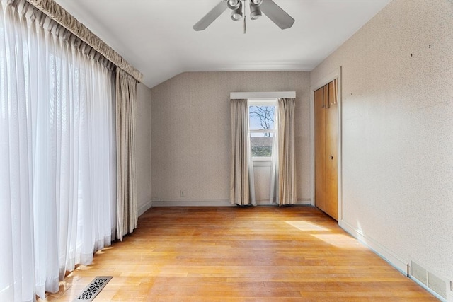 spare room featuring visible vents, light wood-style floors, and vaulted ceiling