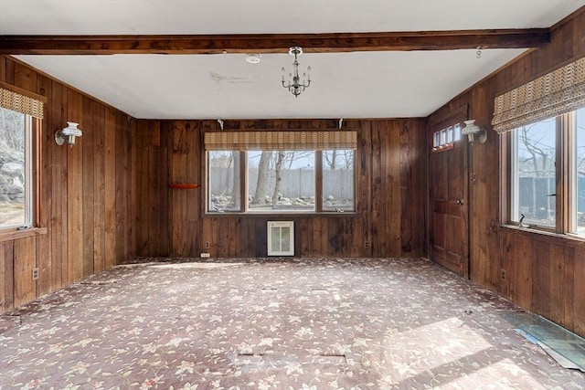 empty room featuring beamed ceiling, carpet floors, wooden walls, and a notable chandelier