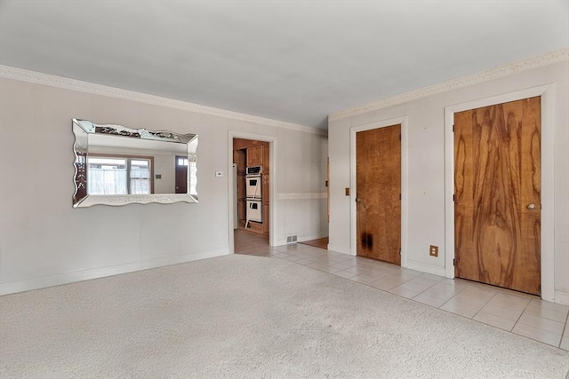 carpeted empty room featuring tile patterned flooring, visible vents, baseboards, and ornamental molding