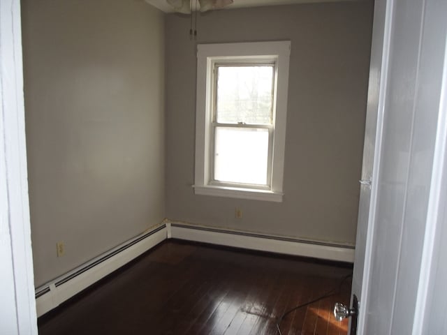 empty room with dark hardwood / wood-style flooring and a baseboard heating unit