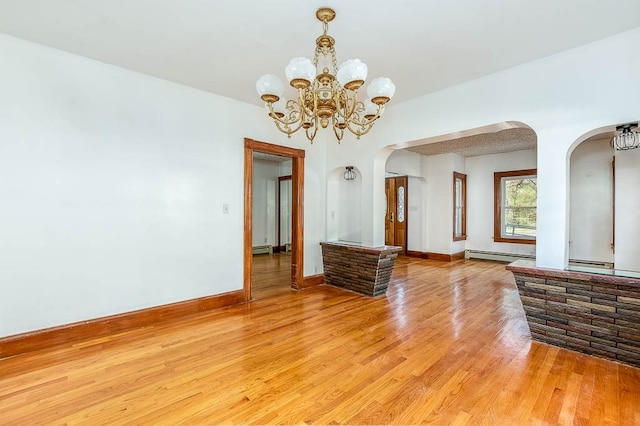 empty room featuring light wood-type flooring, a baseboard radiator, and a notable chandelier