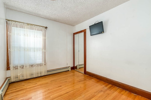 unfurnished room featuring light hardwood / wood-style flooring, a textured ceiling, and a baseboard heating unit