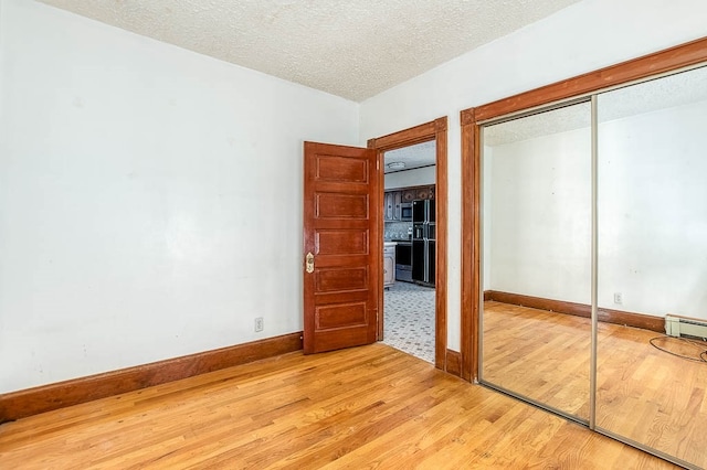 unfurnished bedroom featuring light hardwood / wood-style floors, a textured ceiling, a baseboard heating unit, and a closet