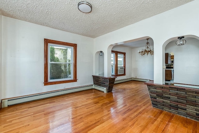 unfurnished room with light wood-type flooring, a textured ceiling, baseboard heating, and a notable chandelier