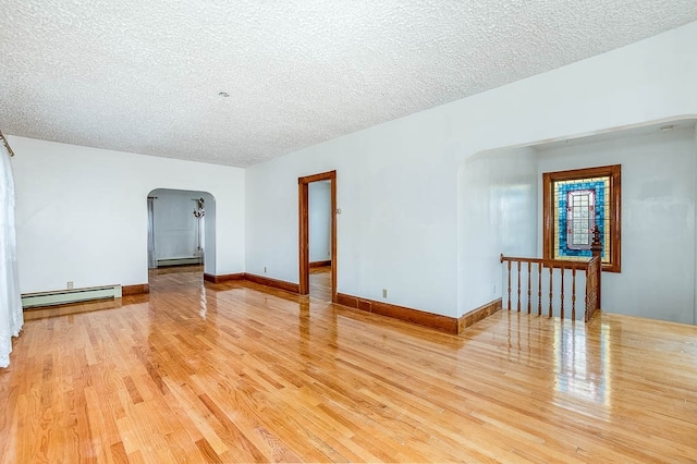 empty room with a textured ceiling, baseboard heating, and light hardwood / wood-style flooring