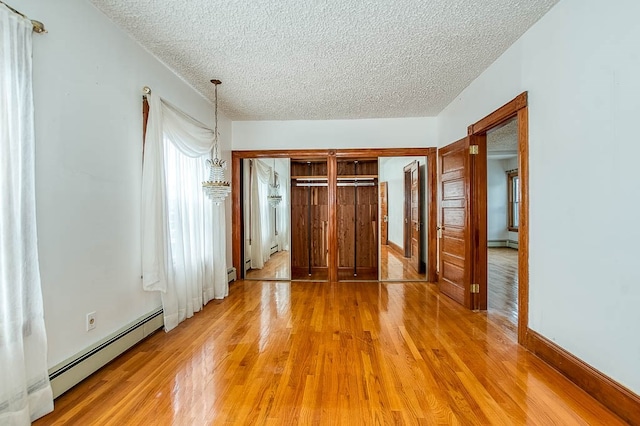 unfurnished bedroom with a textured ceiling, baseboard heating, hardwood / wood-style flooring, and a closet