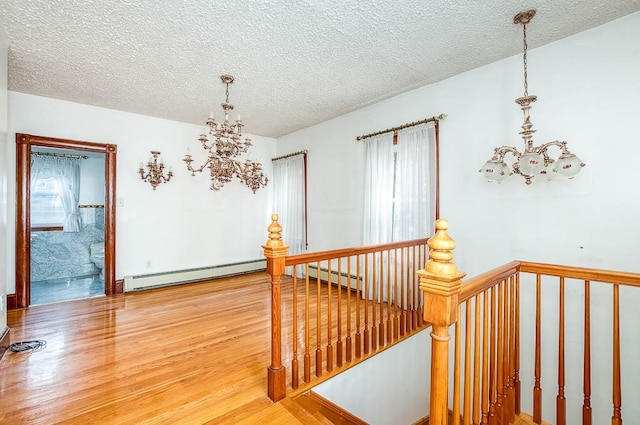 hall with wood-type flooring, a textured ceiling, a baseboard heating unit, and a notable chandelier