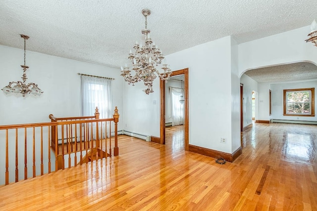 spare room featuring a baseboard heating unit, light wood-type flooring, a textured ceiling, and a chandelier